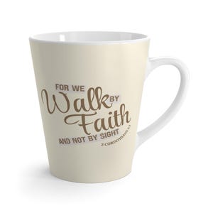 Może przedstawiać: Kubek do kawy w stylu latte z kremowym nadrukiem i białym uchwytem. Kubek zawiera napis "For We Walk by Faith and Not by Sight" brązową czcionką, z wersetem biblijnym 2 Koryntian 5:7.