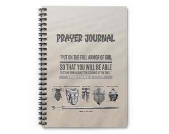 May include: A grey spiral bound prayer journal with the text "PRAYER JOURNAL" in bold, black lettering. The journal features a quote from Ephesians 6:11-17, "PUT ON THE FULL ARMOR OF GOD, SO THAT YOU WILL BE ABLE TO STAND FIRM AGAINST THE SCHEMES OF THE DEVIL." The quote is in black text and is surrounded by a black and white illustration of the armour of God.