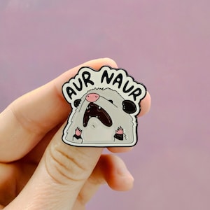 Könnte beinhalten: Ein weiß-grauer Emaille-Pin, der ein Opossum-Cartoon-Motiv mit rosa Nase und Pfoten zeigt. Das Tier hat den Mund weit geöffnet, darüber steht der Text AUR NAUR in schwarzen Buchstaben. Der Pin hat eine schwarze Metallumrandung.