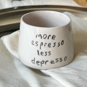 May include: White ceramic mug with black handwritten text that reads "more espresso less depresso".