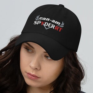 May include: Black baseball cap with the text "can-am SPYDER RT" in white and red. The cap has a curved brim and an adjustable strap at the back. The hat is made of a soft material.