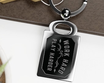 Puede incluir: Llavero de plata con una etiqueta rectangular negra que dice "Work Hard Play Harder" con un gráfico estilizado de una persona corriendo.