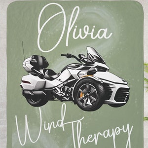 May include: A green and white throw blanket with a white motorcycle illustration and the text "Olivia Wind Therapy".