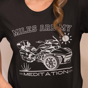 K&ouml;nnte beinhalten: Schwarzes T-Shirt mit dem wei&szlig;en Text "MILES ARE MY MEDITATION" &uuml;ber und unter einer wei&szlig;en Grafik eines dreir&auml;drigen Motorrads und einer Sonne. Das Shirt hat einen Rundhalsausschnitt.