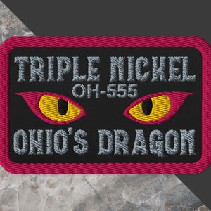 May include: Embroidered patch with a black background and a magenta border. The text "TRIPLE NICKEL OH-555 OHIO'S DRAGON" is displayed in gray. Two stylized yellow and red dragon eyes are in the center.