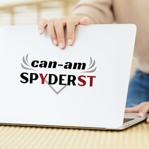 May include: A white laptop computer with the text "can-am SPYDERST" in black and gray lettering on the screen.