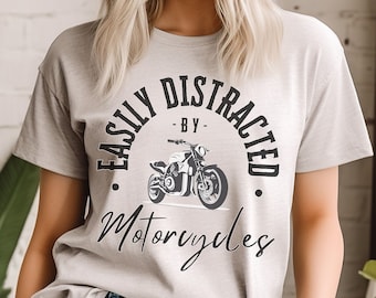 Puede incluir: Una camiseta gris con el texto "Easily Distracted - By - Motorcycles" en letras negras. La camiseta presenta una ilustración en blanco y negro de una motocicleta.