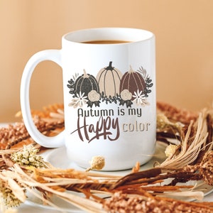 May include: White ceramic mug with a brown, black, and beige illustration of pumpkins and fall foliage. The text "Autumn is my happy color" is printed on the mug.