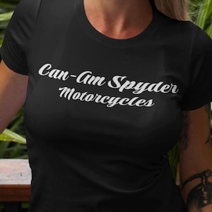 May include: Black crew neck t-shirt with the text "Can-Am Spyder Motorcycles" in white script. The shirt is short-sleeved and made of a soft material. The shirt is worn by a person.
