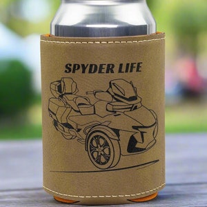 May include: A tan leatherette can cooler with the words "SPYDER LIFE" and a black graphic of a three-wheeled motorcycle. The cooler has orange accents and holds a silver can.