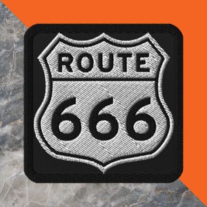 May include: Embroidered patch featuring the iconic Route 666 sign. The design includes a white shield with the word "ROUTE" above the number "666" in bold, black lettering. The patch has a black border and a textured appearance.