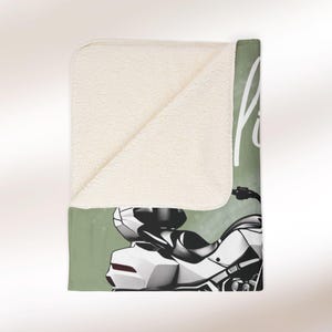 May include: A green and white fleece blanket featuring a motorcycle illustration and the text "Ride" on it.