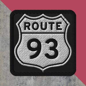 May include: Embroidered patch featuring the iconic Route 93 road sign. The sign is white with black text and a black border, set against a textured background. The text "ROUTE" is above the number "93".