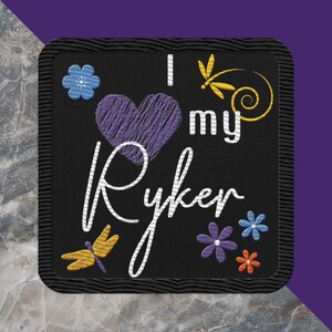 May include: Black embroidered patch with a purple heart, white text that says "I love my Ryker", and yellow and blue floral accents.
