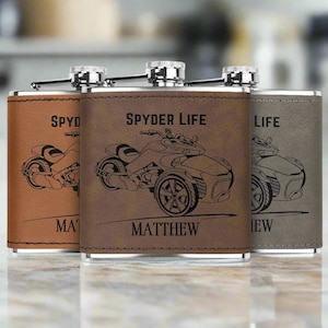 Pu&ograve; includere: Tre fiaschette in acciaio inossidabile rivestite in pelle marrone con un'illustrazione in bianco e nero di una motocicletta a tre ruote. Le fiaschette sono incise con il testo "Spyder Life", "Matthew" e "Life".