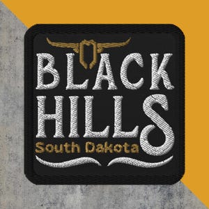 May include: Embroidered patch with the words "BLACK HILLS" in white, arched over "South Dakota" in gold. A gold emblem sits above the text. The patch is black with a black border and a gray and yellow background.