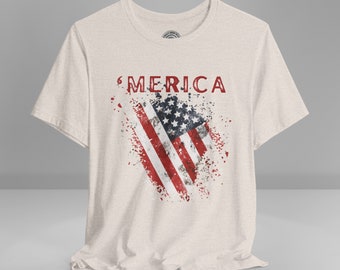 May include: A light beige t-shirt with a distressed American flag graphic and the word "MERICA" printed in red.
