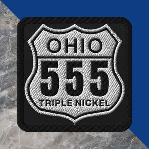 May include: A square embroidered patch with a black background and a white shield-shaped border. The patch features the text OHIO at the top, the number 555 in the center, and the text TRIPLE NICKEL at the bottom, all in black embroidery.