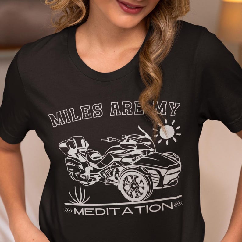 K&ouml;nnte beinhalten: Schwarzes T-Shirt mit dem wei&szlig;en Text "MILES ARE MY MEDITATION" &uuml;ber und unter einer wei&szlig;en Grafik eines dreir&auml;drigen Motorrads und einer Sonne. Das Shirt hat einen Rundhalsausschnitt.