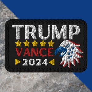 May include: Embroidered patch with the words "TRUMP VANCE 2024" in white and red, with five gold stars and a patriotic eagle design. The patch is rectangular with a black border.