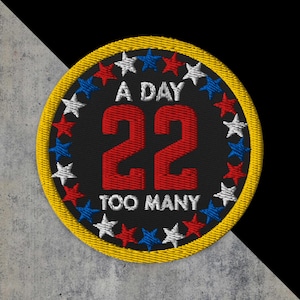 May include: Embroidered patch with a black background, a yellow border, and the text "A DAY 22 TOO MANY" in white and red. The patch is decorated with red, white, and blue stars around the edge.