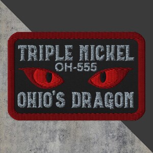 May include: A black and red embroidered patch with the text "Triple Nickel OH-555 Ohio's Dragon". The patch features two red eyes with black pupils.