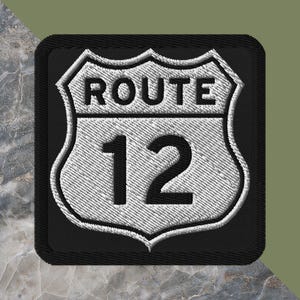 May include: Embroidered patch featuring a Route 12 sign. The sign is white with black text and a black border. The patch has a textured appearance, with the words "ROUTE" above the number "12". The patch is square-shaped.