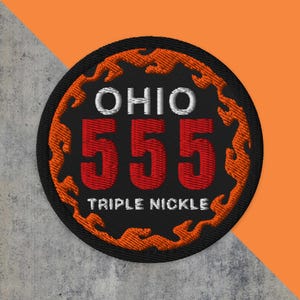 May include: Embroidered patch with a black background, featuring the word "OHIO" in white, the number "555" in red, and the text "TRIPLE NICKLE" in white. An orange flame design surrounds the text.