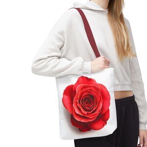 Op de afbeelding: Een witte tote bag met een rode roos bedrukt op de voorkant. De roos is in volle bloei en heeft een witte achtergrond.