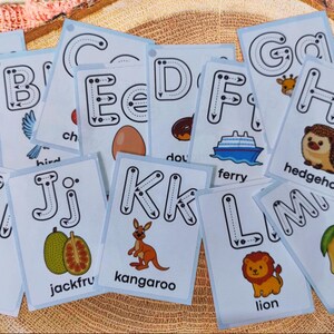Peut inclure: Ensemble de cartes d'alphabet avec des illustrations colorées. Chaque carte présente une lettre, une image et un mot à tracer. Les cartes incluent une pomme, un oiseau, un œuf, un ferry, un hérisson, un impala, un jacquier, un kangourou, un lion et une mangue.