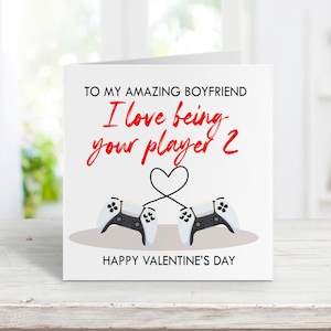 May include: A white Valentine's Day card with the text "TO MY AMAZING BOYFRIEND, I love being your player 2" in red script. Two game controllers are connected by a heart. The words "HAPPY VALENTINE'S DAY" are at the bottom.
