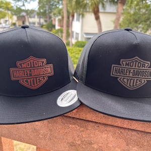 Puede incluir: Dos gorras de camionero negras con el logotipo de Harley-Davidson Cycles. El logotipo tiene forma de escudo con las palabras "MOTOR HARLEY-DAVIDSON CYCLES". Las gorras tienen la parte trasera de malla y cierre snapback.