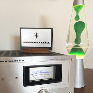 Puede incluir: Un amplificador est&eacute;reo Marantz plateado con una pantalla de medidor en blanco y negro y una perilla plateada etiquetada como "ganancia derecha". El amplificador tiene una etiqueta negra que dice "amplificador est&eacute;reo de potencia".