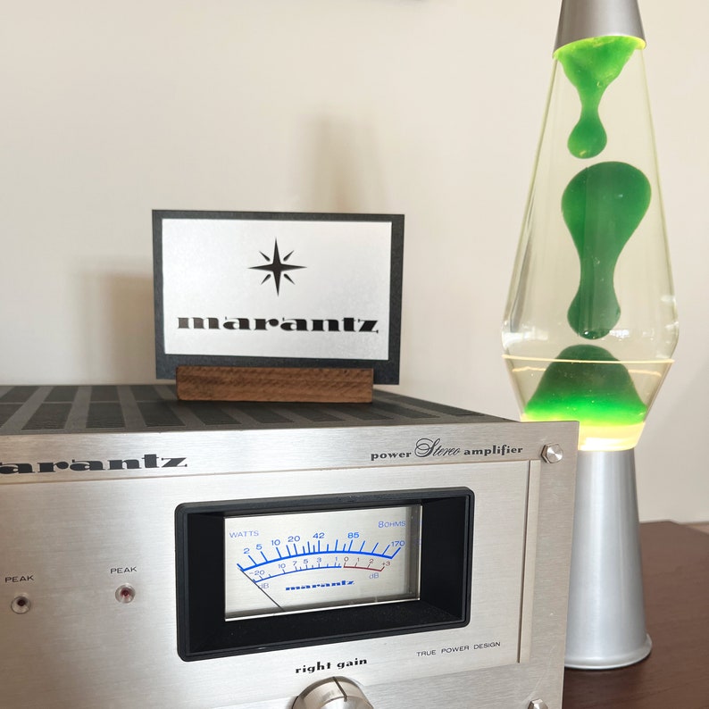 Puede incluir: Un amplificador est&eacute;reo Marantz plateado con una pantalla de medidor en blanco y negro y una perilla plateada etiquetada como "ganancia derecha". El amplificador tiene una etiqueta negra que dice "amplificador est&eacute;reo de potencia".