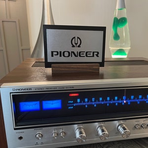 K&ouml;nnte beinhalten: Ein Vintage-Stereo-Receiver Pioneer GX-630 mit silberner und schwarzer Frontplatte und einem Holzkasten. Der Receiver verf&uuml;gt &uuml;ber ein blaues digitales Display und eine Reihe silberner Kn&ouml;pfe zum Einstellen des Klangs.