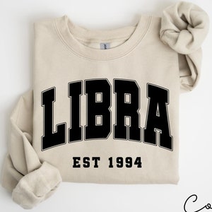 May include: A beige sweatshirt with black text that reads "LIBRA EST 1994".