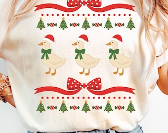 May include: Ivory-colored Christmas-themed sweatshirt featuring three cartoon ducks wearing Santa hats and green bows. The design includes red bows, Christmas trees, and candy canes. The text "Color Ivory" is at the bottom.
