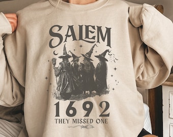 May include: A beige sweatshirt with a vintage-style graphic of three witches with the text "Salem 1692 They Missed One" printed on the front.