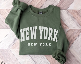 May include: A green sweatshirt with the text "NEW YORK" in white letters. The text "NEW YORK" is repeated in smaller letters below the larger text.