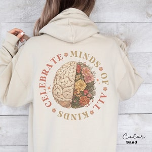 May include: Sand-colored hoodie with a circular graphic on the back. The graphic features a detailed brain illustration on the left and a floral arrangement on the right, with the text "CELEBRATE MINDS OF ALL KINDS" in a circular pattern around the brain.