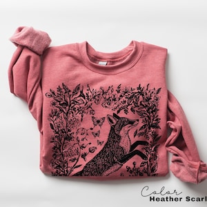 Pu&ograve; includere: Felpa rosso scarlatto melange con un'illustrazione di una volpe nera circondata da elementi floreali e farfalle. La volpe &egrave; raffigurata in un disegno stilizzato e dettagliato. Il testo "Color Heather Scarlet Red" &egrave; in basso.