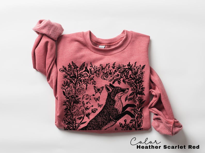 Pu&ograve; includere: Felpa rosso scarlatto melange con un'illustrazione di una volpe nera circondata da elementi floreali e farfalle. La volpe &egrave; raffigurata in un disegno stilizzato e dettagliato. Il testo "Color Heather Scarlet Red" &egrave; in basso.