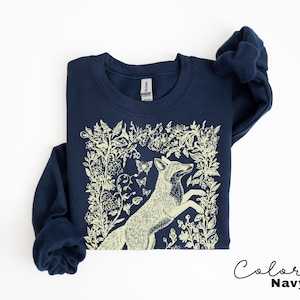 Pu&ograve; includere: Felpa blu navy con un'illustrazione di volpe color crema circondata da elementi floreali e farfalle. Il testo "Color Navy" &egrave; scritto in corsivo in basso a destra. La felpa &egrave; uno stile girocollo.