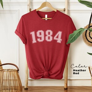 May include: Red heather t-shirt with the year 1984 printed in pink on the front.