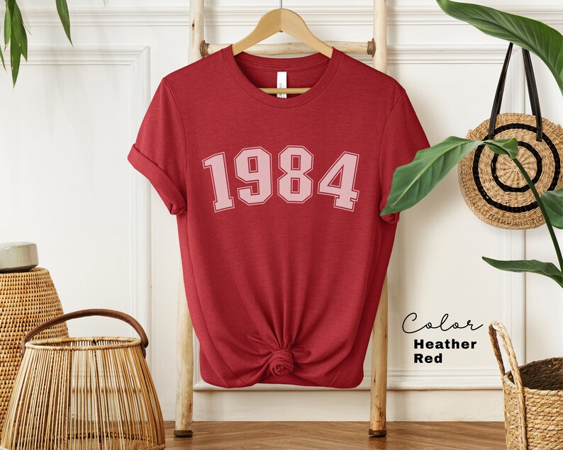 May include: Red heather t-shirt with the year 1984 printed in pink on the front.