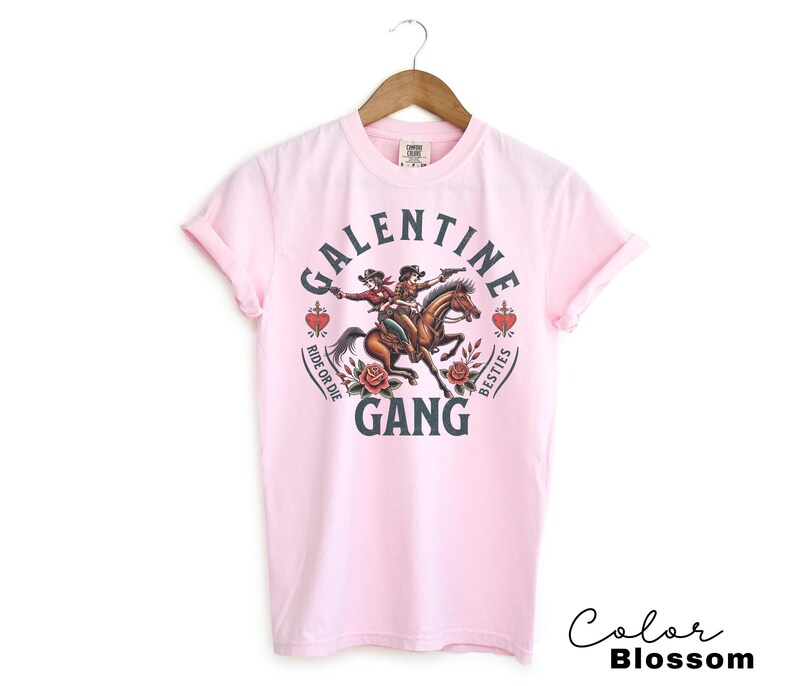 May include: Light pink t-shirt with a graphic that reads "Galentine Gang" with two women riding a horse. The design includes roses, hearts, and the phrases "Ride or Die" and "Besties". The words "Color Blossom" are written in cursive.