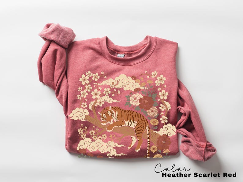 May include: Heather scarlet red sweatshirt with a tiger graphic. The design features a tiger resting on a tree branch, surrounded by flowers and clouds. The text "Color Heather Scarlet Red" is at the bottom.