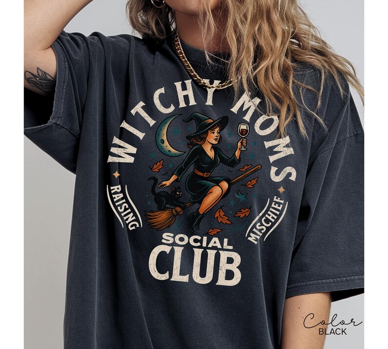Puede incluir: Camiseta negra con un dise&ntilde;o circular. Presenta una bruja en una escoba sosteniendo una copa de vino, un gato negro y el texto "Witchy Moms Social Club". El dise&ntilde;o incluye una luna creciente y hojas de oto&ntilde;o.