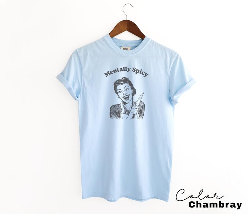 Puede incluir: Camiseta azul claro con un gr&aacute;fico de una mujer sosteniendo un cuchillo y el texto "Mentally Spicy".