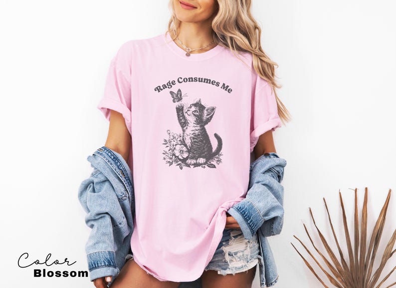 May include: A pink t-shirt with a black and white illustration of a cat looking up at a butterfly. The text "Rage Consumes Me" is printed on the shirt.